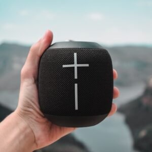 a hand holding a black speaker with a cross on it