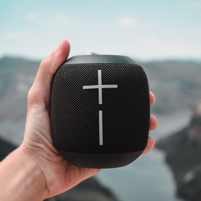 a hand holding a black speaker with a cross on it